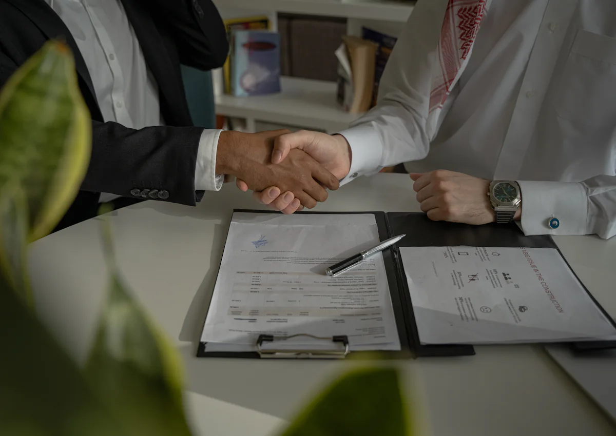 Two business partners shaking hands over a signed agreement